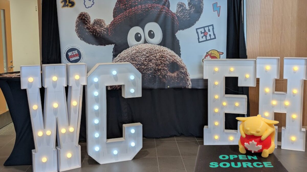 Wapuu holding a red ball with a maple leaf, sitting on an "open source" cube in front of the "WCEH" letters.